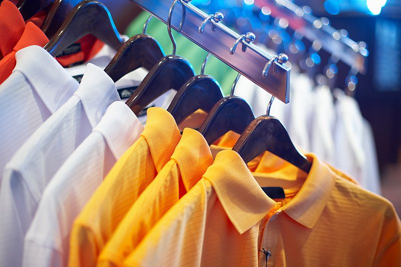 Rack of blank polos in white, orange and yellow ready to be decorated