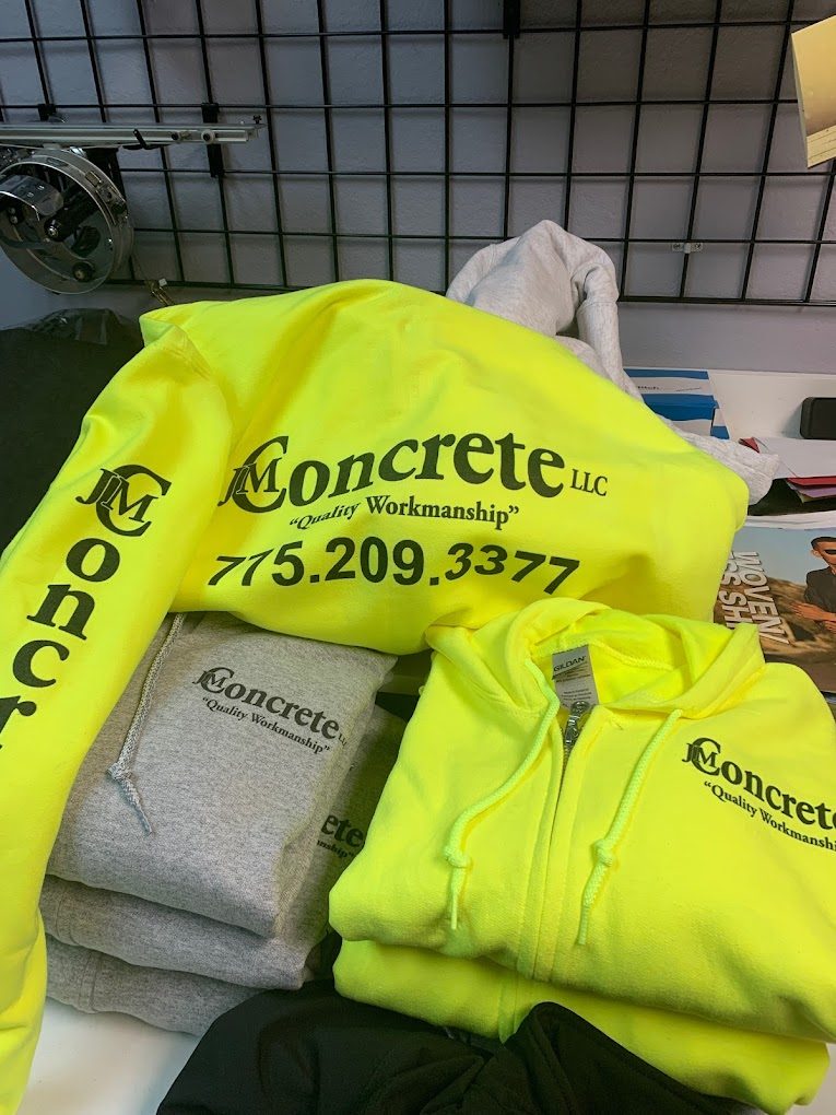 Stack of hi-vis yellow hoodies and shirts printed with the JM Concrete logo